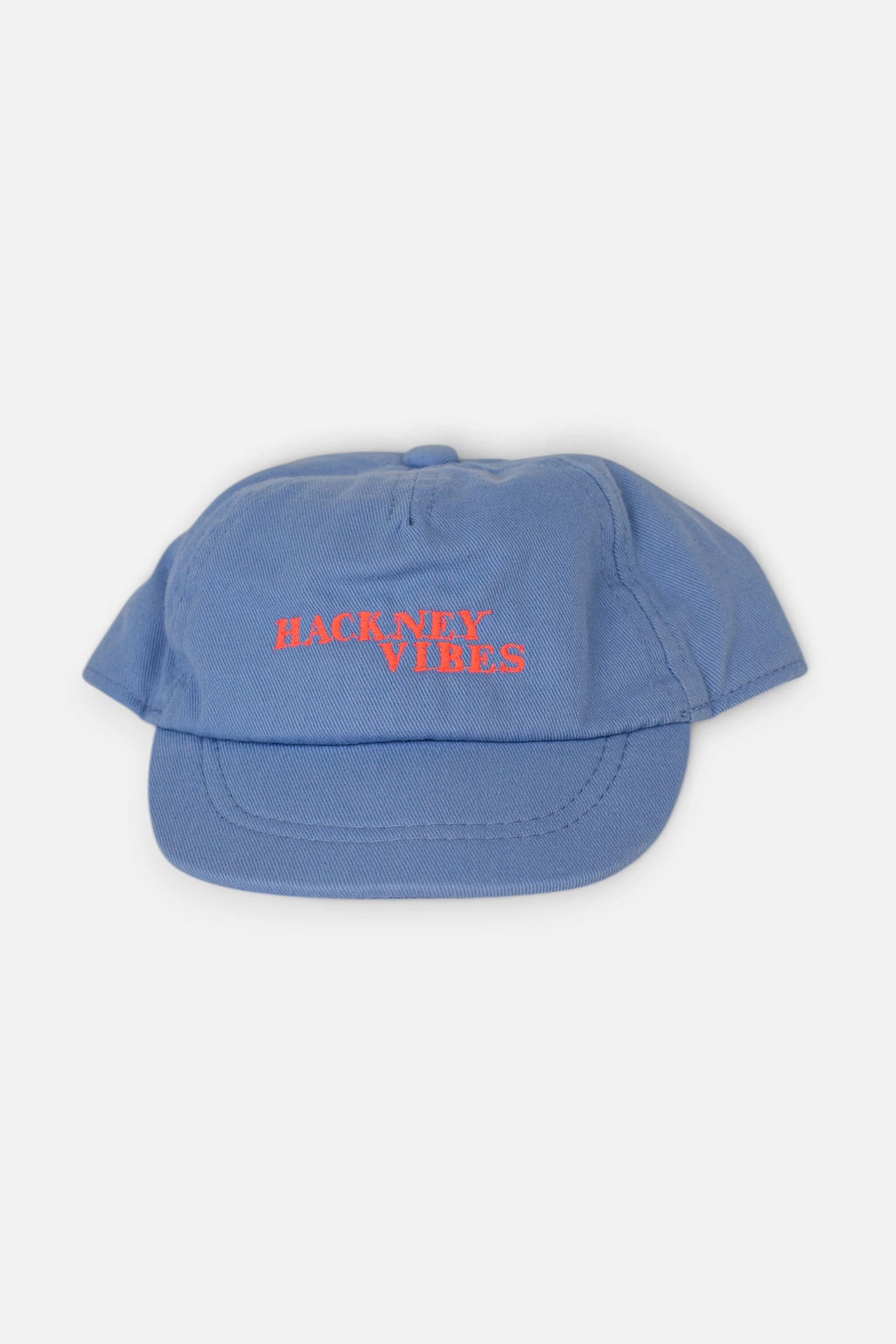 A light blue baseball cap with 'HACKNEY VIBES' embroidered in fluorescent coral orange across the front, shown against a plain light grey background.