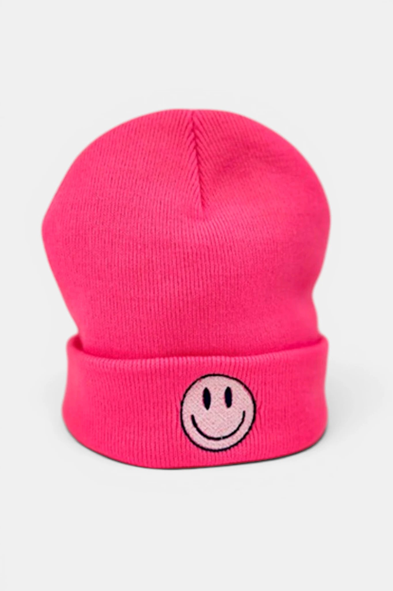 A fluorescent pink beanie hat with a folded cuff featuring a small embroidered smiley face patch in the center, shown against a light gray background.