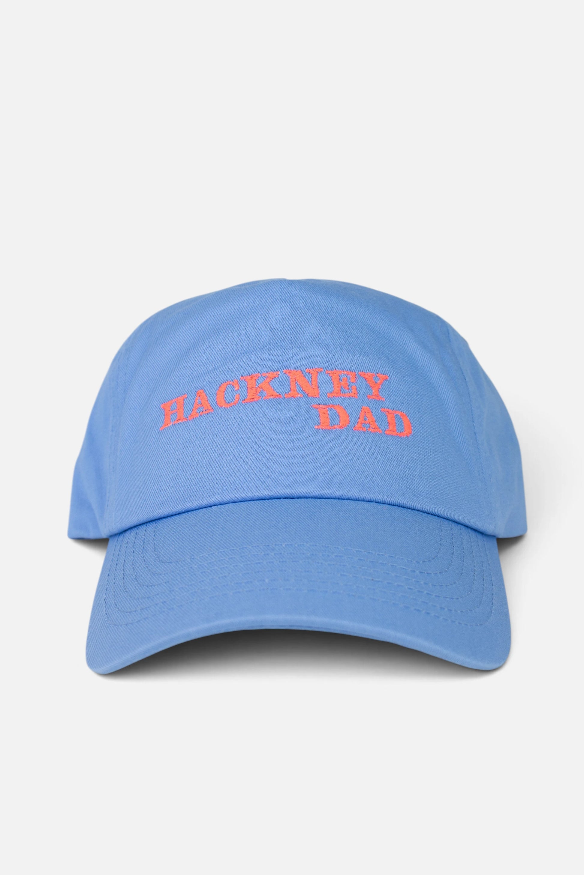 A light blue baseball cap with 'HACKNEY DAD' embroidered in fluorescent coral orange text across the front, shown against a plain light grey background.