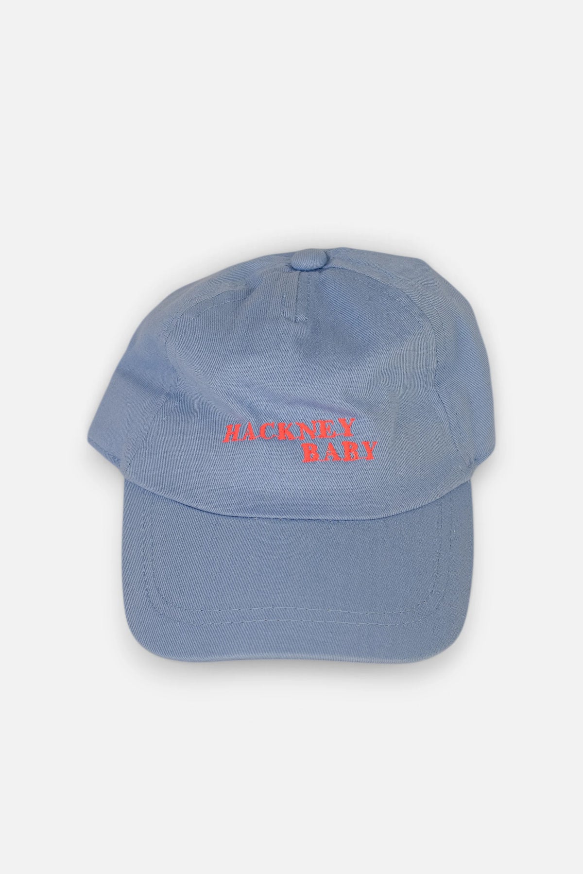 A light blue cotton toddler baseball cap with 'HACKNEY BABY' embroidered in fluorescent coral orange across the front, shown against a plain light grey background.
