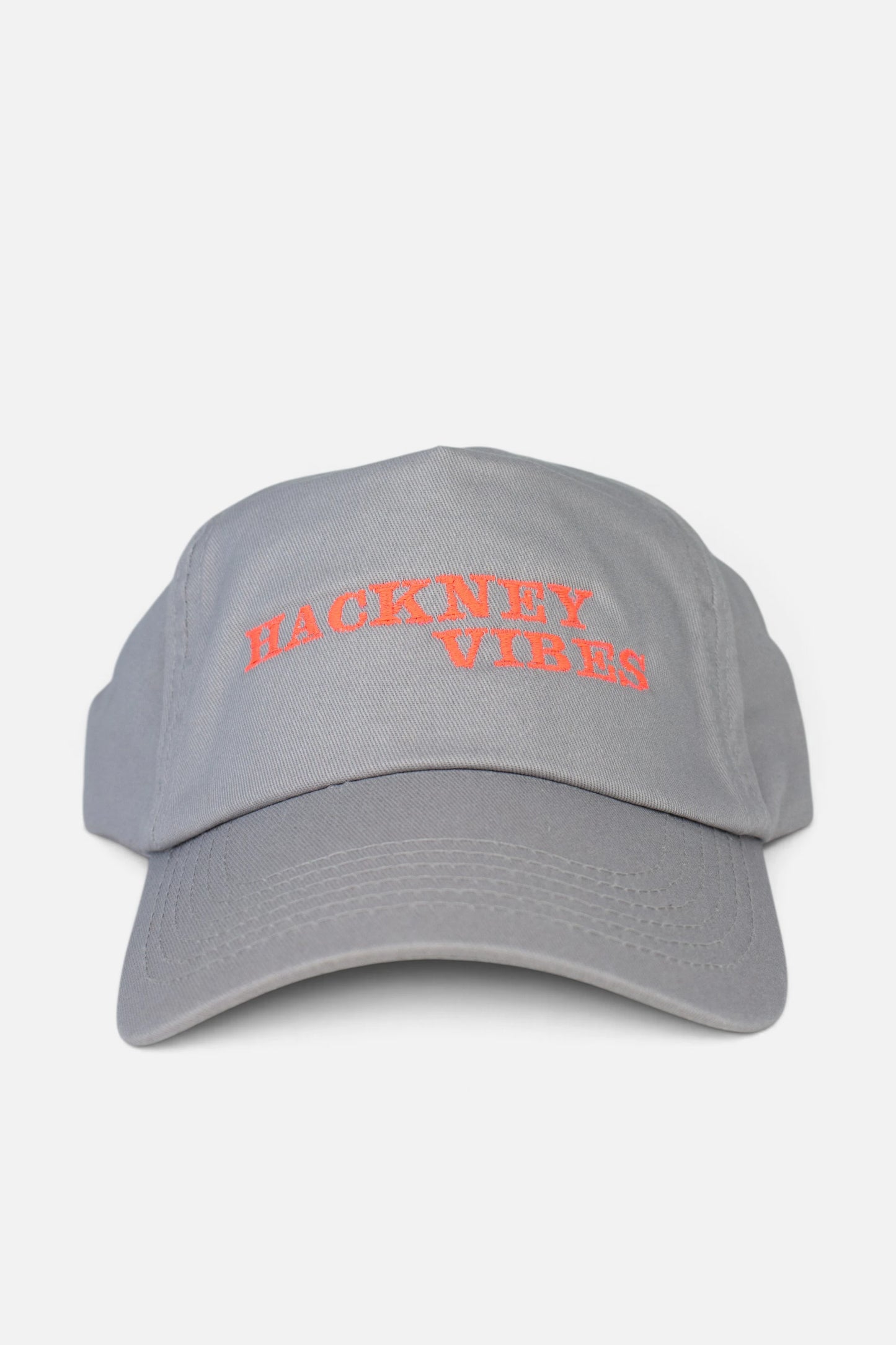 A light grey baseball cap with 'HACKNEY VIBES' embroidered in fluorescent coral orange across the front, shown against a plain light grey background.