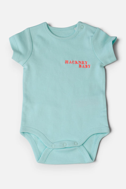 A mint green baby bodysuit with short sleeves and a fluorescent coral orange 'HACKNEY BABY' logo embroidered on the chest, displayed flat against a light grey background.