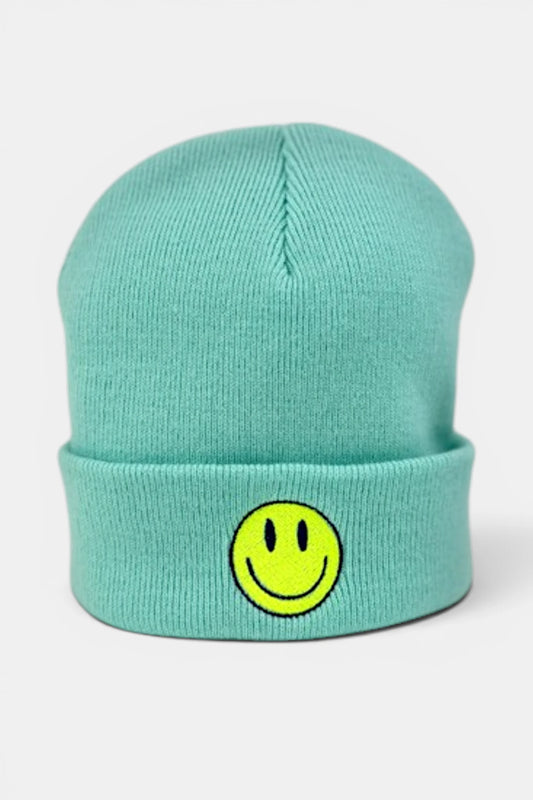 A mint green beanie hat featuring a yellow smiley face patch on the front cuff, set against a plain light gray background.