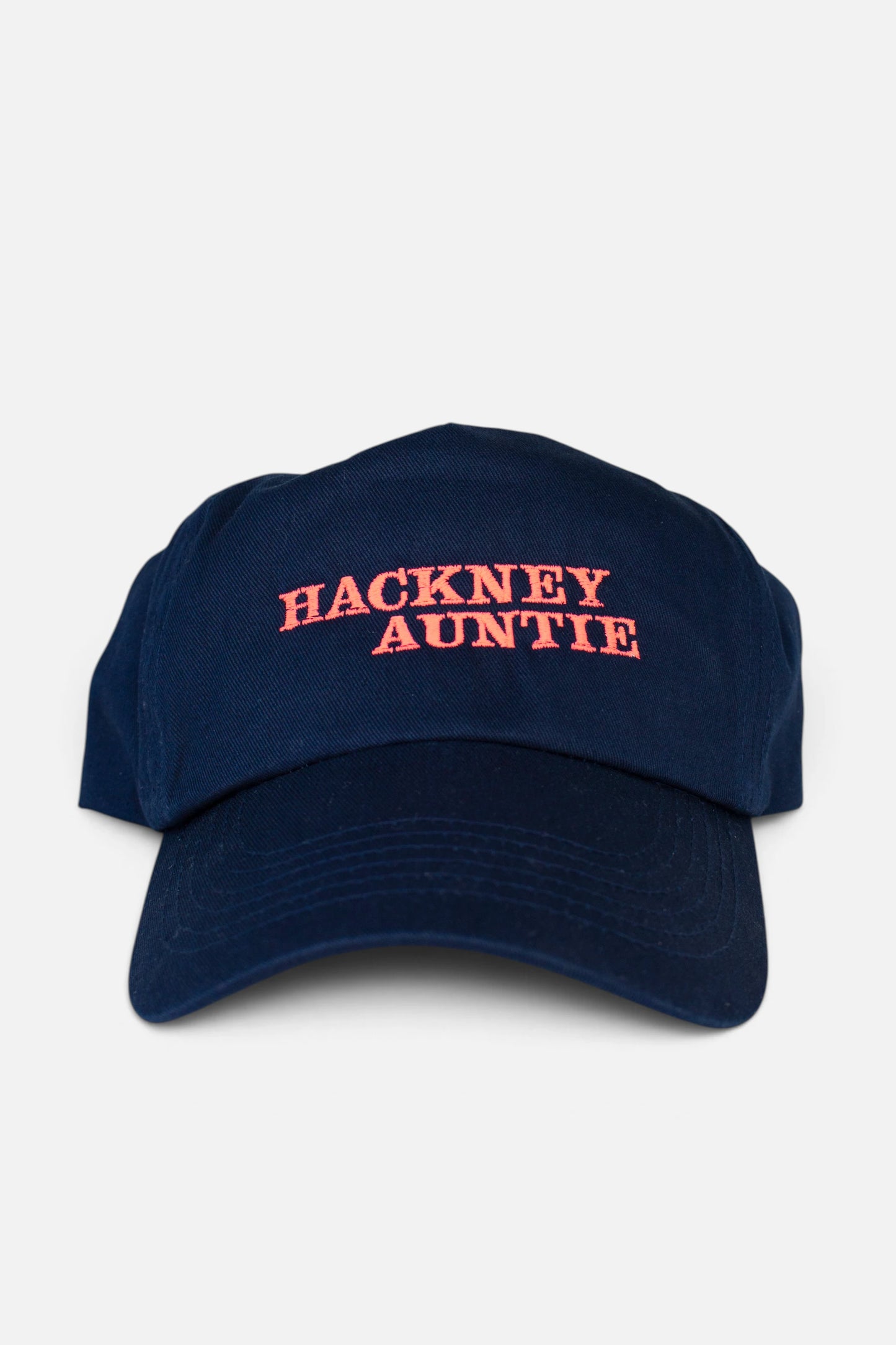 A navy blue baseball cap with 'HACKNEY AUNTIE' embroidered in fluorescent coral orange text on the front, set against a plain light grey background.