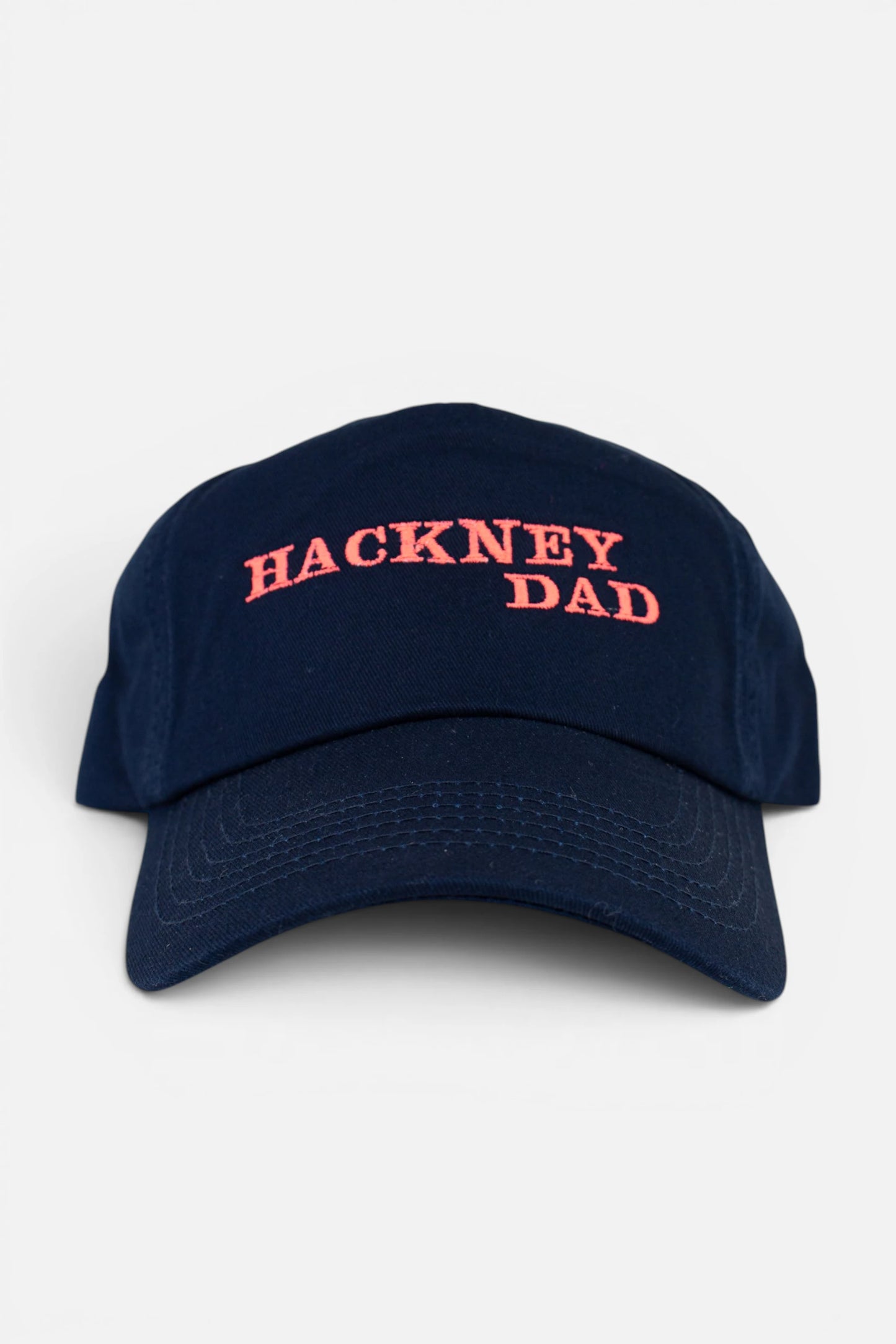 Navy Blue Hackney Dad cap with fluorescent coral orange embroidery, photographed on a neutral light grey background.