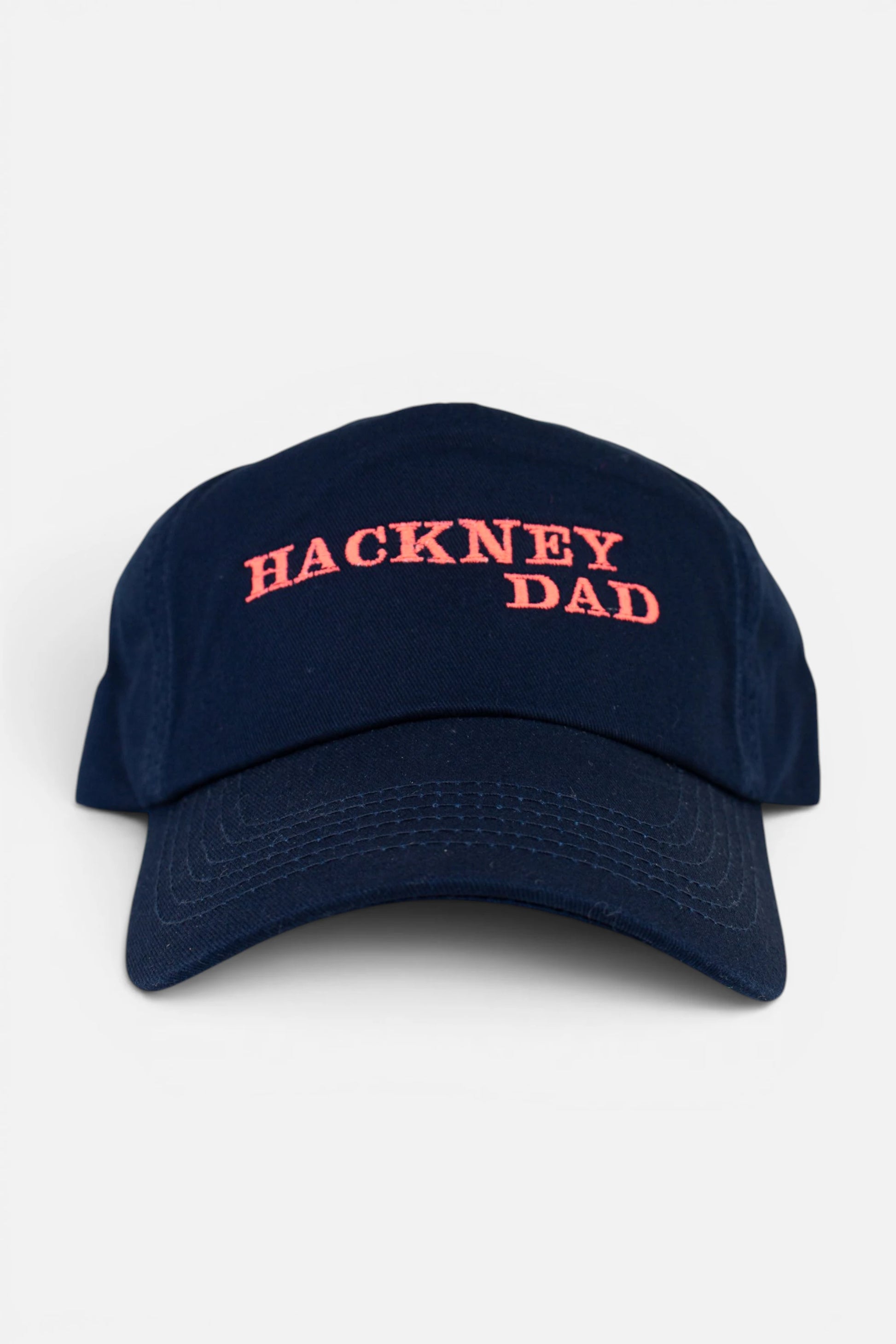 Navy Blue Hackney Dad cap with fluorescent coral orange embroidery, photographed on a neutral light grey background.
