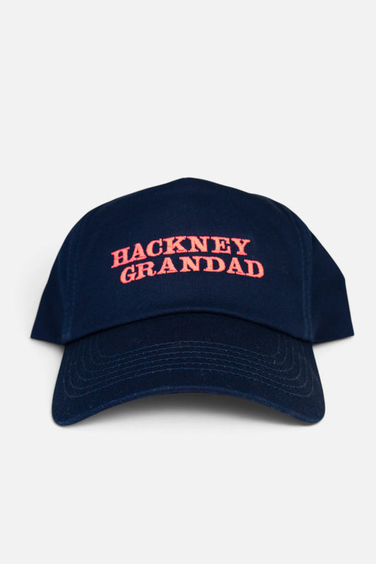 A navy blue baseball cap with 'HACKNEY GRANDAD' embroidered in fluorescent coral orange across the front, set against a plain light grey background.
