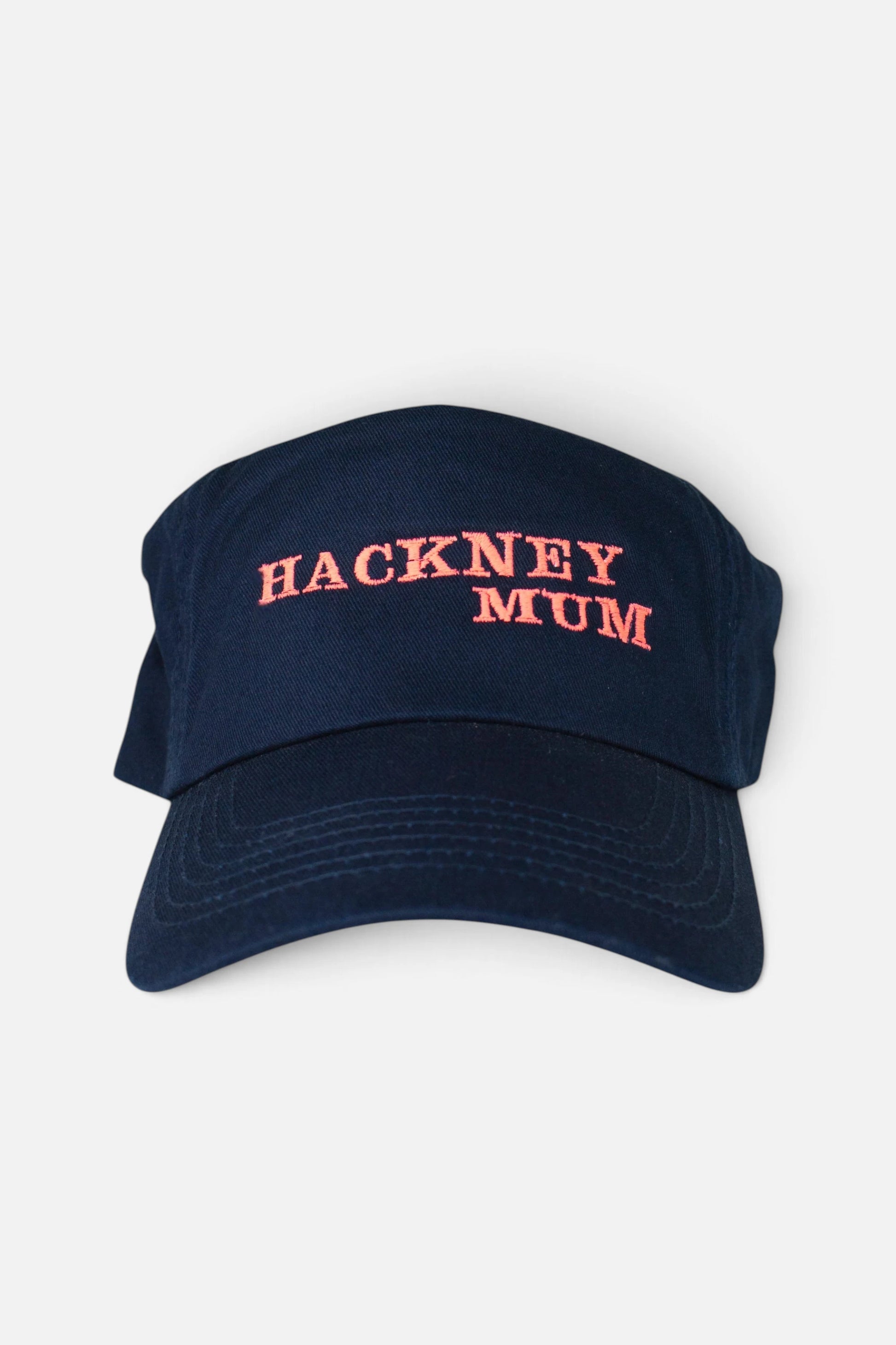 A navy blue baseball cap with 'HACKNEY MUM' embroidered in fluorescent coral orange lettering on the front, shown against a plain light grey background.