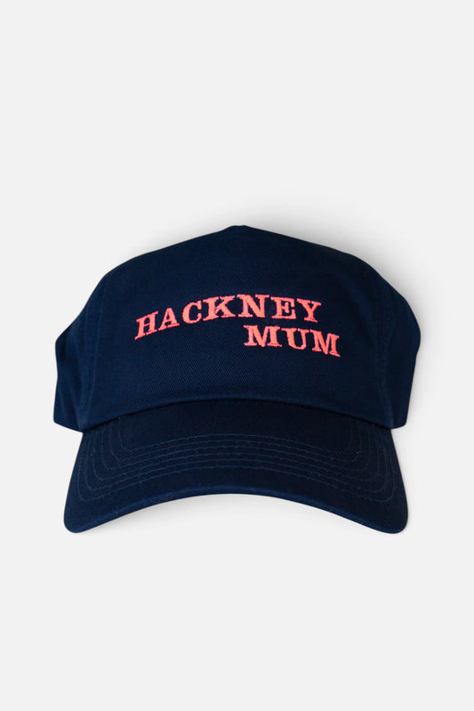 A navy blue baseball cap with 'HACKNEY MUM' embroidered in fluorescent coral orange across the front, shown against a plain light grey background.
