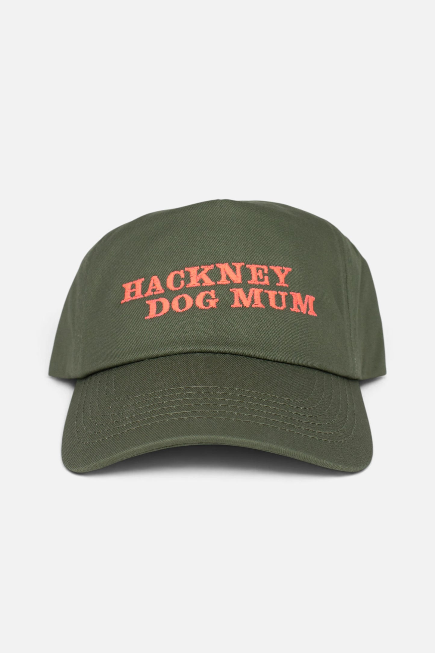 An olive green baseball cap with 'HACKNEY DOG MUM' embroidered in coral-orange text on the front, shown against a plain light grey background.