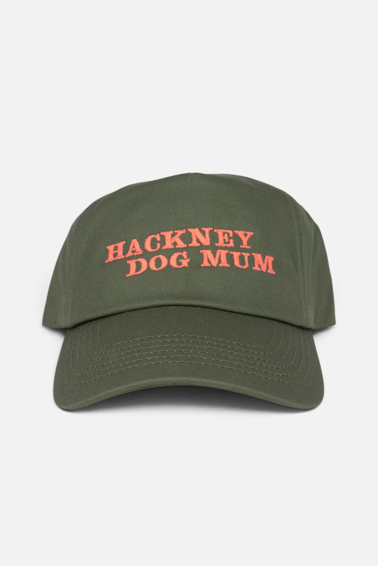 An olive green baseball cap with 'HACKNEY DOG MUM' embroidered in coral-orange text on the front, shown against a plain light grey background.
